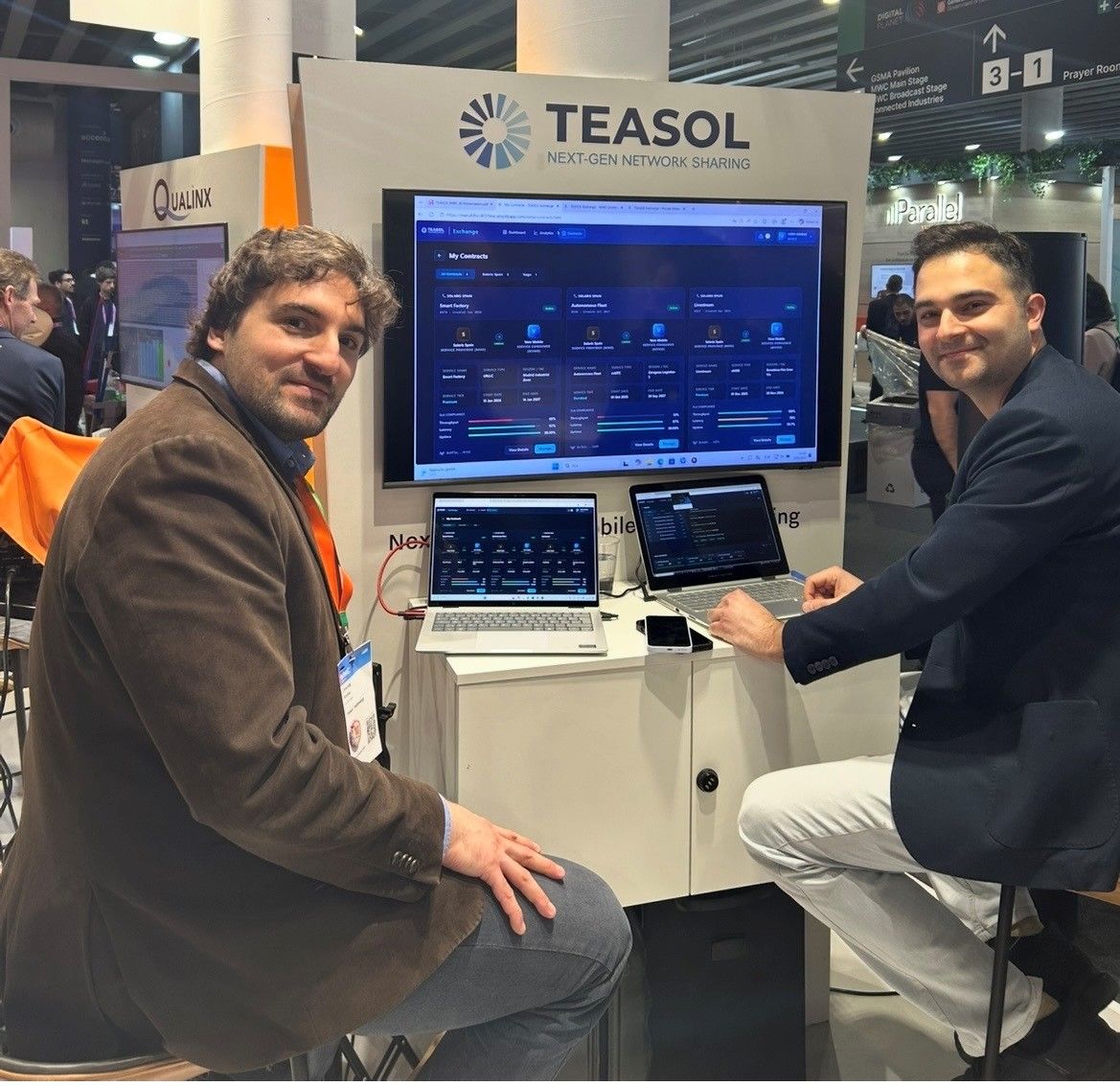 Two of the team at the TEASOL stand at MWC 2026, with the Exchange dashboard on the main screen